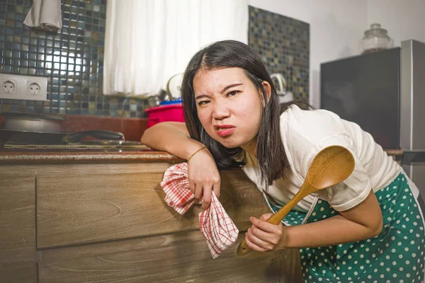 Young tired and stressed Asian Chinese woman in cook apron working leaning on kitchen sink lazy in moody and upset face housekeeping at home and crying — Stock Photo, Image