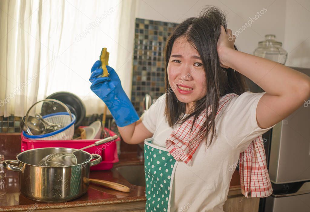 domestic chores lifestyle portrait of young tired and stressed Asian Korean woman in cook apron washing dishes at kitchen sink working lazy in moody and upset face doing housework