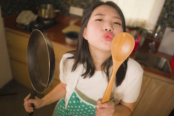 Ung vacker och lycklig asiatisk kinesisk kvinna hemma i förkläde håller matlagning Pan och sked lekfull leende njuter inhemska sysslor — Stockfoto