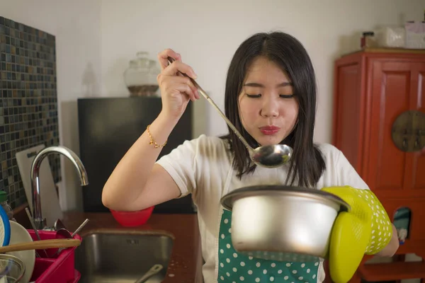 Asiatique cuisine maison fille style de vie portrait. Jeune femme chinoise heureuse et belle dans le tablier de cuisine et le gant tenant le pot de cuisson excité et satisfait préparant la soupe ravie — Photo