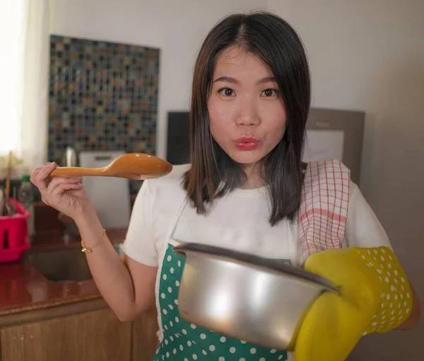 Asiatico casa cuoco ragazza stile di vita ritratto. Giovane donna cinese felice e bella in cucina grembiule e guanto tenendo pentola eccitata e soddisfatta preparare la zuppa deliziata — Foto Stock