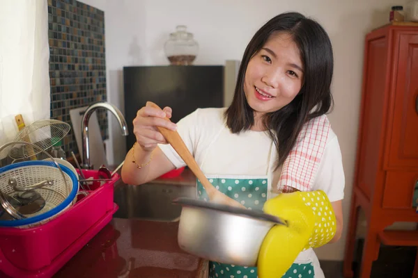 Asiatico casa cuoco ragazza stile di vita ritratto. Giovane donna cinese felice e bella in cucina grembiule e guanto tenendo pentola eccitata e soddisfatta preparare la zuppa deliziata — Foto Stock