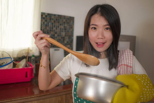 Asiatico casa cuoco ragazza stile di vita ritratto. Giovane donna coreana felice e bella in cucina grembiule e guanto tenendo pentola eccitata e soddisfatta preparare la zuppa deliziata — Foto Stock