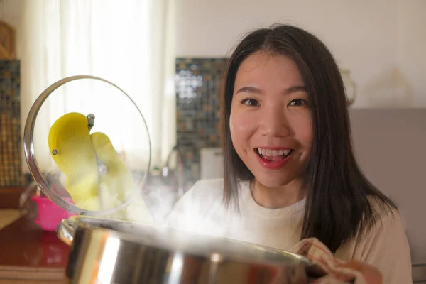 Asiatique cuisine maison fille style de vie portrait. Jeune femme coréenne heureuse et belle dans le tablier de cuisine et le gant tenant le pot de cuisson excité et satisfait préparant la soupe — Photo