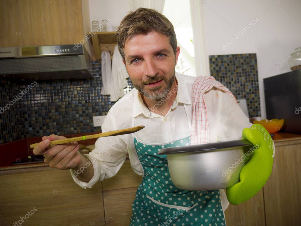Stile di vita domestico ritratto di uomo felice e attraente in cucina  grembiule e guanto tenendo pentola eccitato con delizioso sapore di zuppa  in cuoco di successo a casa - Foto Stock