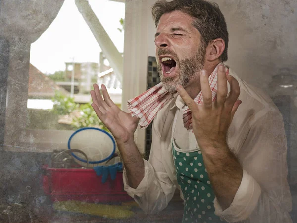 Dramatisches Grunge-Porträt eines Hausmannes oder alleinstehenden Mannes in Küchenschürze, der Hausarbeit erledigt, Geschirr spült oder im Stress kocht und frustriert und verzweifelt schreit — Stockfoto