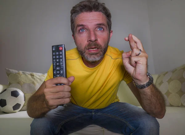 stressed man watching football game on TV sitting at home living room couch excited and with expression of crazy intense emotion enjoying soccer match