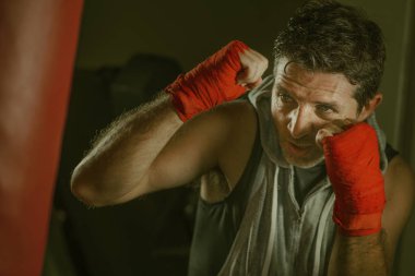 fitness kulübünde genç çekici ve şiddetli görünümlü adam eğitim boks yaşam tarzı spor salonu portre badass savaşçı bakmak bilek sarar ile ağır çanta delme egzersiz yapıyor 
