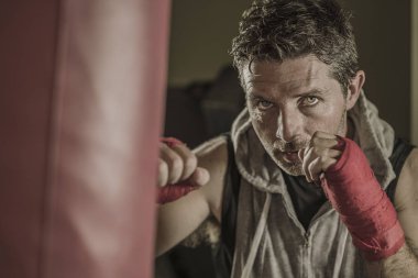fitness kulübünde genç çekici ve şiddetli görünümlü adam eğitim boks yaşam tarzı spor salonu portre badass savaşçı bakmak bilek sarar ile ağır çanta delme egzersiz yapıyor 