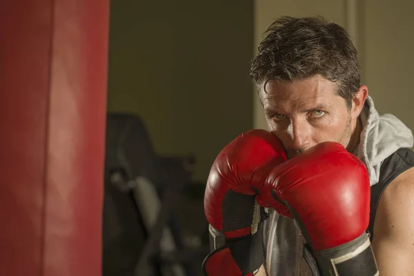 Fitnesstraining Portrait eines attraktiven und grimmig aussehenden Boxers der 30er bis 40er Jahre in Boxhandschuhen beim Training im Fitness-Club Boxsack im coolen und bösartigen Kämpfer-Look — Stockfoto