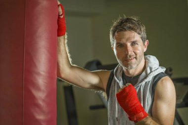 genç mutlu ve terli adam spor salonunda boks ağır çanta üzerinde kapüşonlu yelek eğitim boks terli dışarı çalışma savaşçı bilek sarar serin gülümseyen görünümlü