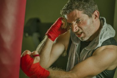 fitness kulübünde genç çekici ve şiddetli görünümlü adam eğitim boks yaşam tarzı spor salonu portre badass savaşçı bakmak bilek sarar ile ağır çanta delme egzersiz yapıyor 