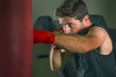 fitness kulübünde genç çekici ve şiddetli görünümlü adam eğitim boks yaşam tarzı spor salonu portre badass savaşçı bakmak bilek sarar ile ağır çanta delme egzersiz yapıyor 