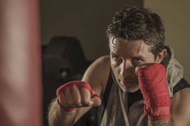 fitness kulübünde genç çekici ve şiddetli görünümlü adam eğitim boks yaşam tarzı spor salonu portre badass savaşçı bakmak bilek sarar ile ağır çanta delme egzersiz yapıyor 