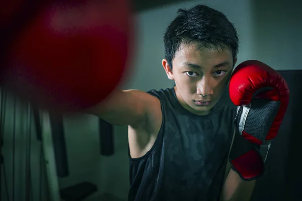 Unga stilig och hård tonåring pojke gör Fight Workout stansning tung väska ser cool och badass på Fitness Club utbildning hårt med handskar — Stockfoto