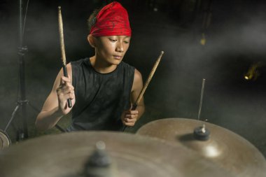 Genç rock grubu davulcusu . serin ve yetenekli Asya Amerikalı karışık etnik genç çocuk karanlık sisli sahnede şarkı performans kafa bandı davul çalıyor