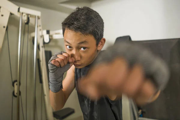 Asiatisch-amerikanischer Teenager boxt im Fitnessstudio. Portrait des jungen hübschen und grimmigen 13 oder 14 Jahre alten Jungen in Handgelenkwickeln beim Kampf-Workout, der in harter Haltung cool aussieht — Stockfoto