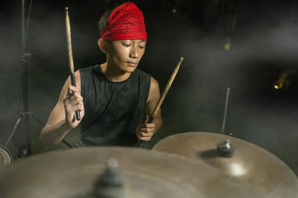 Барабанщик подростковой рок-группы. классный и талантливый азиатско-американский смешанный этнос подросток, играющий на барабанах в головном уборе, исполняя песню на темной туманной сцене — стоковое фото