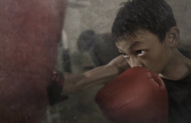 Sert ve havalı genç çocuk kum torbasını yumrukluyor. 13-14 yaşlarında Asyalı bir genç Tayland boks antrenmanı yapıyor. Sert bir dövüşçü olarak meydan okuyor.