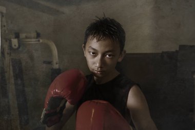 Sert ve havalı genç çocuk kum torbasını yumrukluyor. 13-14 yaşlarında Asyalı bir genç Tayland boks antrenmanı yapıyor. Sert bir dövüşçü olarak meydan okuyor.