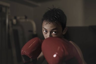 Sert ve havalı genç çocuk kum torbasını yumrukluyor. 13-14 yaşlarında Asyalı bir genç Tayland boks antrenmanı yapıyor. Sert bir dövüşçü olarak meydan okuyor.