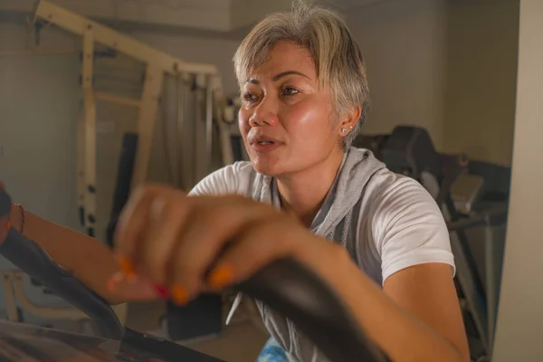 Estilo de vida retrato de mediana edad atractiva y saludable mujer indonesia asiática con ejercicio de entrenamiento de pelo gris en el gimnasio haciendo ejercicio de bicicleta estacionaria sudoroso — Foto de Stock