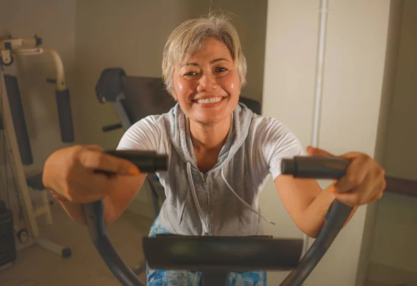 Estilo de vida retrato de mediana edad atractiva y feliz mujer indonesia asiática con ejercicio de entrenamiento de pelo gris sonriendo en el gimnasio haciendo ejercicio de bicicleta estacionaria sudoroso — Foto de Stock
