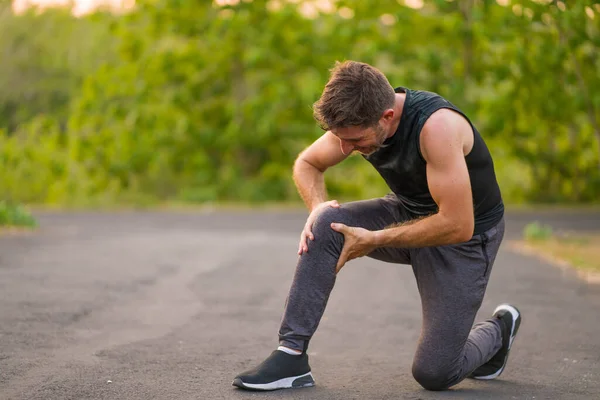 Draußen Porträt eines jungen attraktiven Sportlers, der Schmerzen im Knie hat, Bänderverletzungen hat oder sich beim Lauftraining auf der schönen Landstraße verletzt — Stockfoto