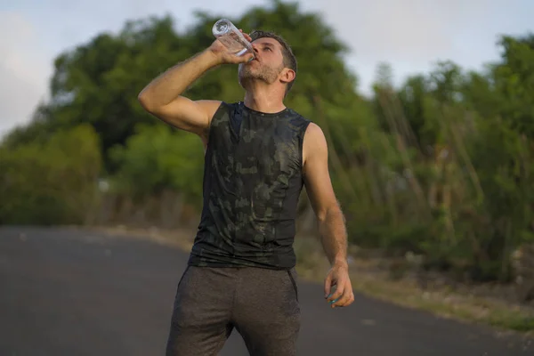 Esporte e fitness estilo de vida retrato de jovem atraente e feliz homem bebendo água cansado e exausto depois de duro ao ar livre corrida treino em bela estrada rural — Fotografia de Stock