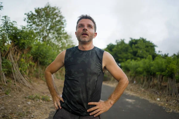 Deporte y fitness estilo de vida retrato de joven atractivo hombre sudoroso y cansado agotado después de correr al aire libre entrenamiento en la respiración hermosa carretera país — Foto de Stock