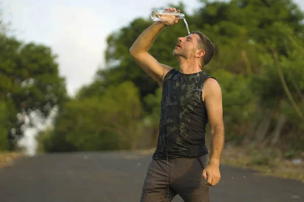 Fitness livsstil porträtt av ung attraktiv och svettig man hälla vatten i ansiktet och dricka utmattad efter hård utomhus löpning träning på vacker landsväg — Stockfoto