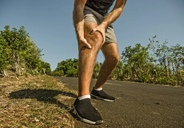 Nahaufnahme Hände und Beine des Sportlers verletzt Berühren seines Knies in Schmerzen leiden körperliche Probleme oder eine Verletzung während des Lauftrainings im Freien in Gesundheitskonzept — Stockfoto