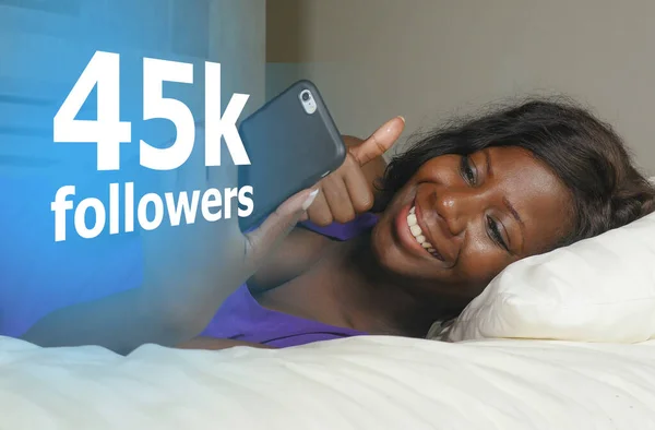 Mujer afroamericana negra feliz acostada relajada en la cama usando el teléfono móvil de Internet sonriendo red alegre consiguiendo seguidores en los medios sociales en estilo de vida influencer exitoso — Foto de Stock