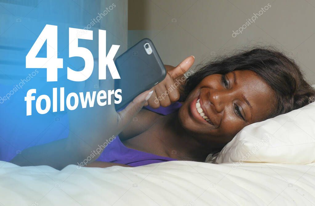 happy black African American woman lying relaxed on bed using internet mobile phone smiling cheerful networking getting social media followers in successful influencer lifestyle