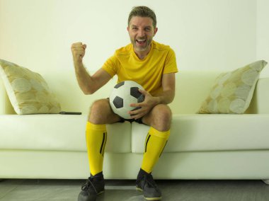 funny and crazy soccer fan man dressed in his team uniform watching football game on television celebrating scoring goal excited screaming spastic and cheering on couch  clipart