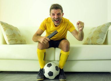funny and crazy soccer fan man dressed in his team uniform watching football game on television celebrating scoring goal excited screaming spastic and cheering on couch  clipart