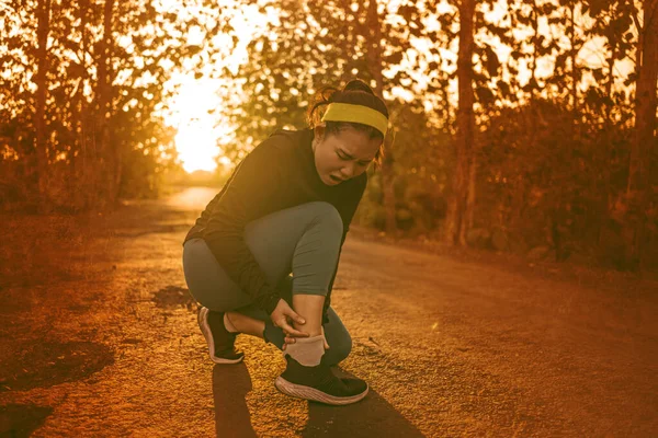 Fitness estilo de vida retrato de jovem atraente mulher corredor asiático sofrendo lesão esportiva durante jogging treino na estrada por do sol segurando tornozelo torcido na dor — Fotografia de Stock