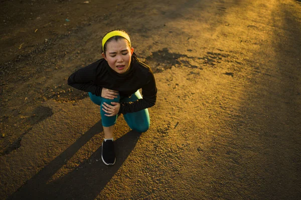 Портрет з фітнесу молодої привабливої азіатської бігуни травмується під час тренування на заході сонця, тримаючи коліно від болю. — стокове фото