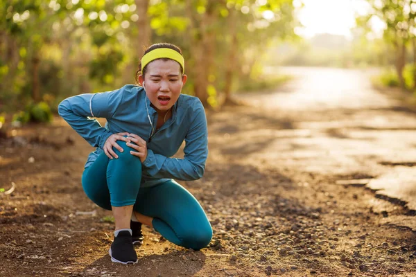 Fitness styl życia portret młodej atrakcyjnej azjatyckiej biegaczki cierpiącej kontuzję sportową podczas treningu joggingowego na Sunset Road trzymającej kolano w bólu — Zdjęcie stockowe