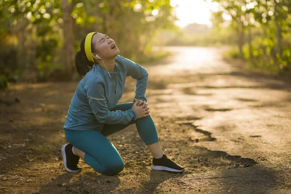 Estilo de vida de fitness retrato de joven corredor asiático atractivo mujer que sufre lesiones deportivas durante el ejercicio de jogging en la carretera puesta del sol sosteniendo la rodilla en el dolor — Foto de Stock