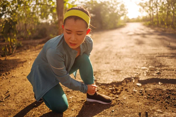 Фитнес-образ жизни портрет молодой привлекательной азиатской бегуньи из Китая, страдающей спортивной травмой во время бега трусцой на закате дороги, держащей вывихнутую лодыжку от боли — стоковое фото