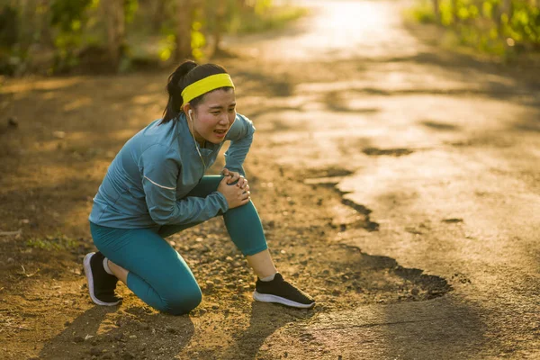 Fitness styl życia portret młodej atrakcyjnej azjatyckiej biegaczki cierpiącej kontuzję sportową podczas treningu joggingowego na Sunset Road trzymającej kolano w bólu — Zdjęcie stockowe