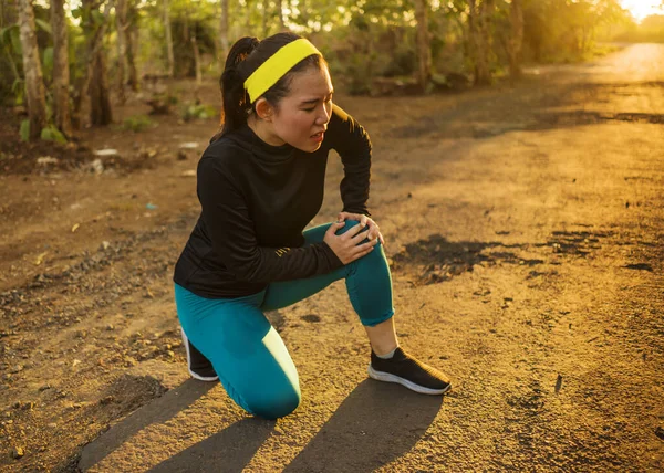 Fitness styl życia portret młodej atrakcyjnej azjatyckiej biegaczki cierpiącej kontuzję sportową podczas treningu joggingowego na Sunset Road trzymającej kolano w bólu — Zdjęcie stockowe