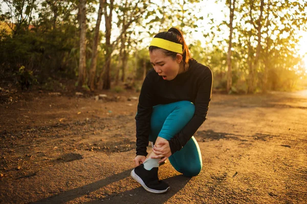 Fitness lifestyle portrait of young attractive Asian runner woman suffering sport injury during jogging workout on sunset road holding twisted ankle in pain — Stok Foto