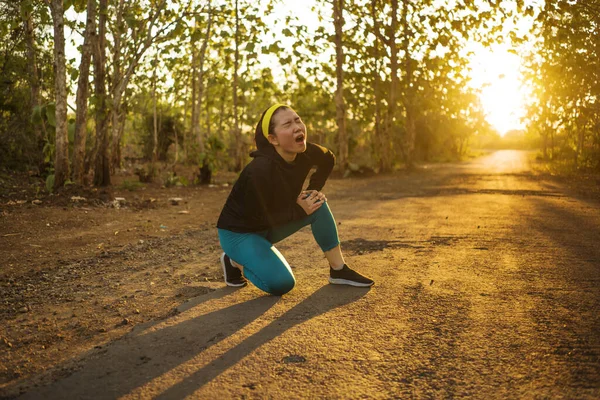 Fitness estilo de vida retrato de jovem atraente mulher corredor asiático sofrendo lesão esportiva durante jogging treino na estrada por do sol segurando joelho na dor — Fotografia de Stock