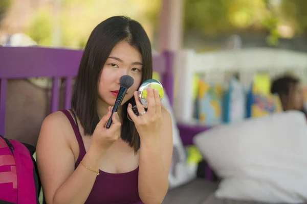 Retrato de estilo de vida natural da jovem bela e feliz mulher chinesa asiática retocando maquiagem antes de uma data ao ar livre no café usando escova e pequeno espelho no conceito de beleza — Fotografia de Stock