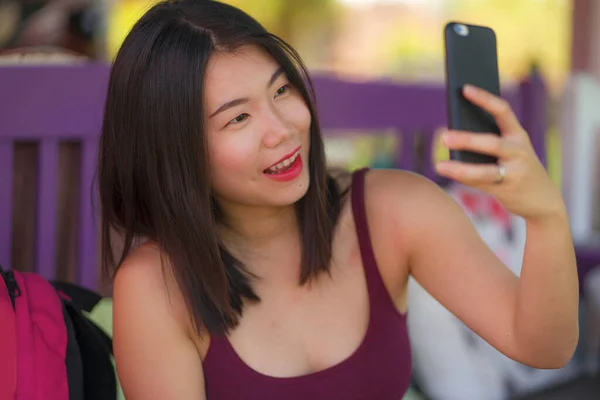 Estilo de vida natural toma de joven hermosa y feliz mujer japonesa asiática tomando foto retrato selfie con teléfono de la mano sonriendo sentado al aire libre disfrutando de vacaciones de verano —  Fotos de Stock