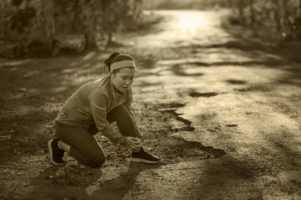 Fitness estilo de vida retrato de jovem atraente mulher corredor asiático sofrendo lesão esportiva durante jogging treino na estrada por do sol segurando tornozelo torcido na dor — Fotografia de Stock