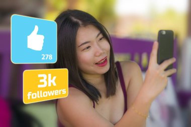 Genç, tatlı ve mutlu Asyalı Çinli kız dışarıda cep telefonuyla selfie çekiyor sosyal medya uygulamaları ve internet takipçileri ikonlarıyla internet blogcusu olarak. 