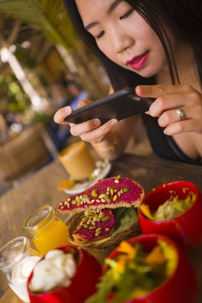 Молодая красивая азиатка фотографирует еду с телефоном для интернет-блога. Корейская девушка выкладывает онлайн фото для вегетарианских органических социальных сетей — стоковое фото
